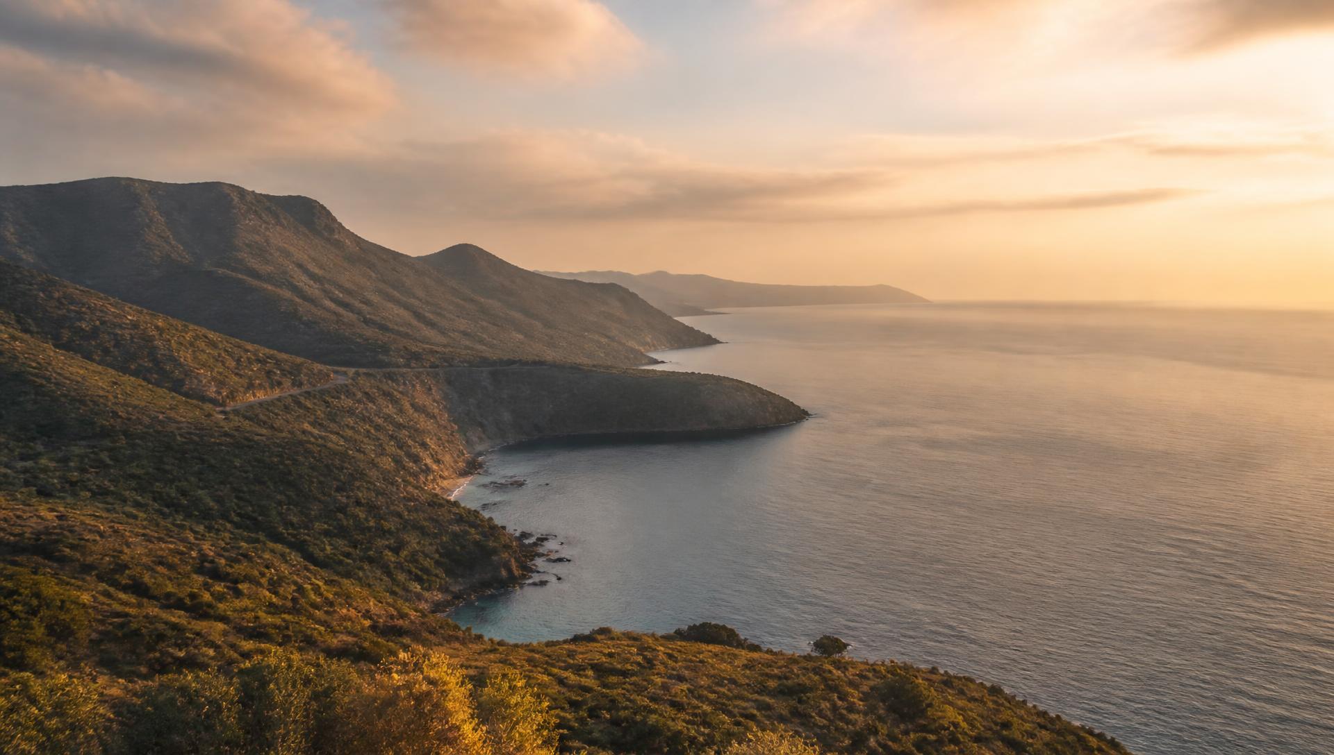 A serene coastal landscape with gentle hills meeting a calm sea at golden hour